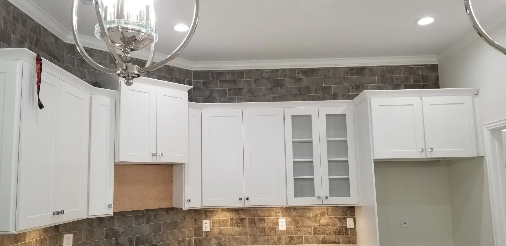 White kitchen cabinets with glass-front doors, mosaic backsplash, and a chandelier overhead