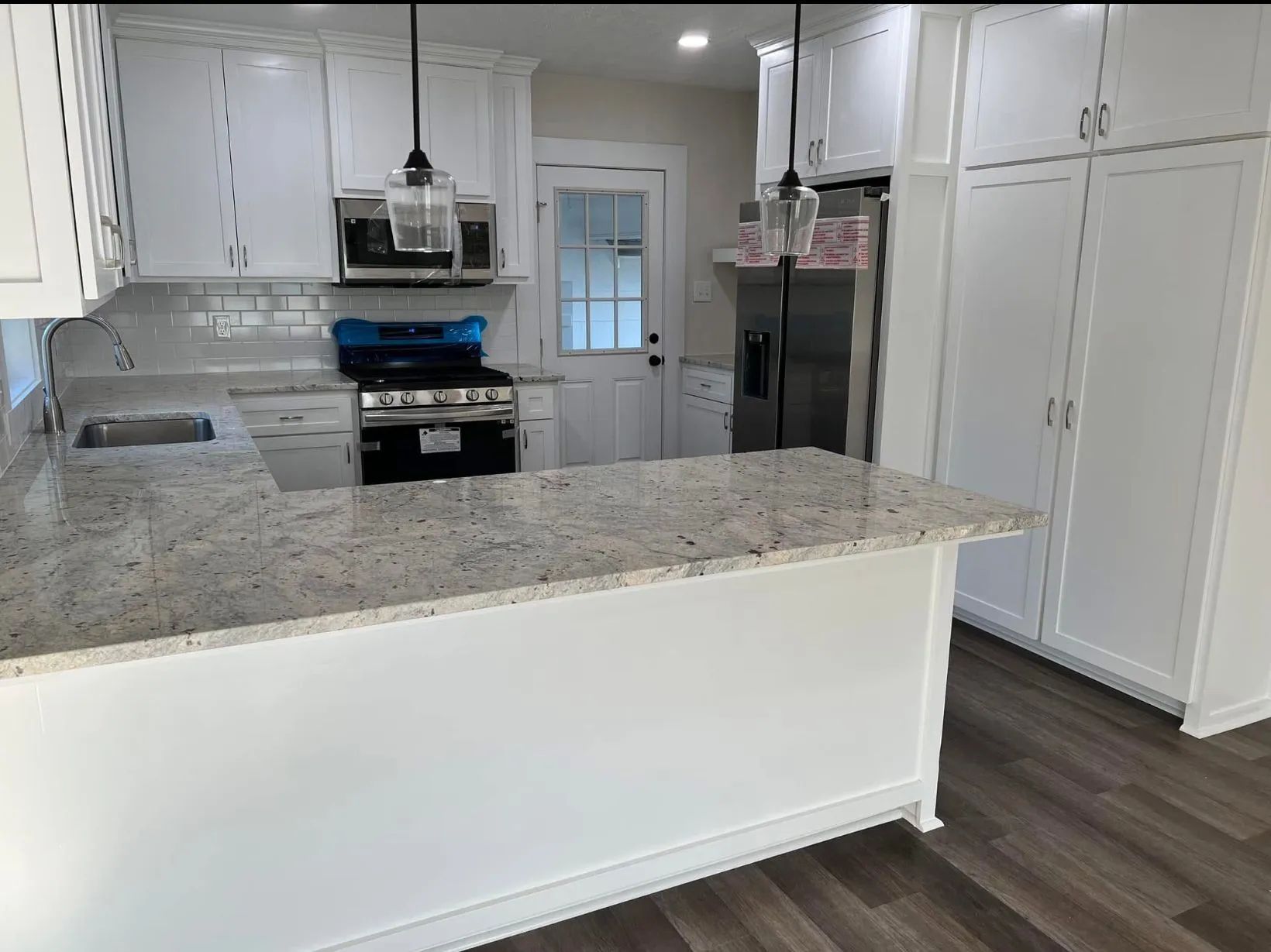 Bright white kitchen with granite island, stainless appliances, and wood-look flooring.