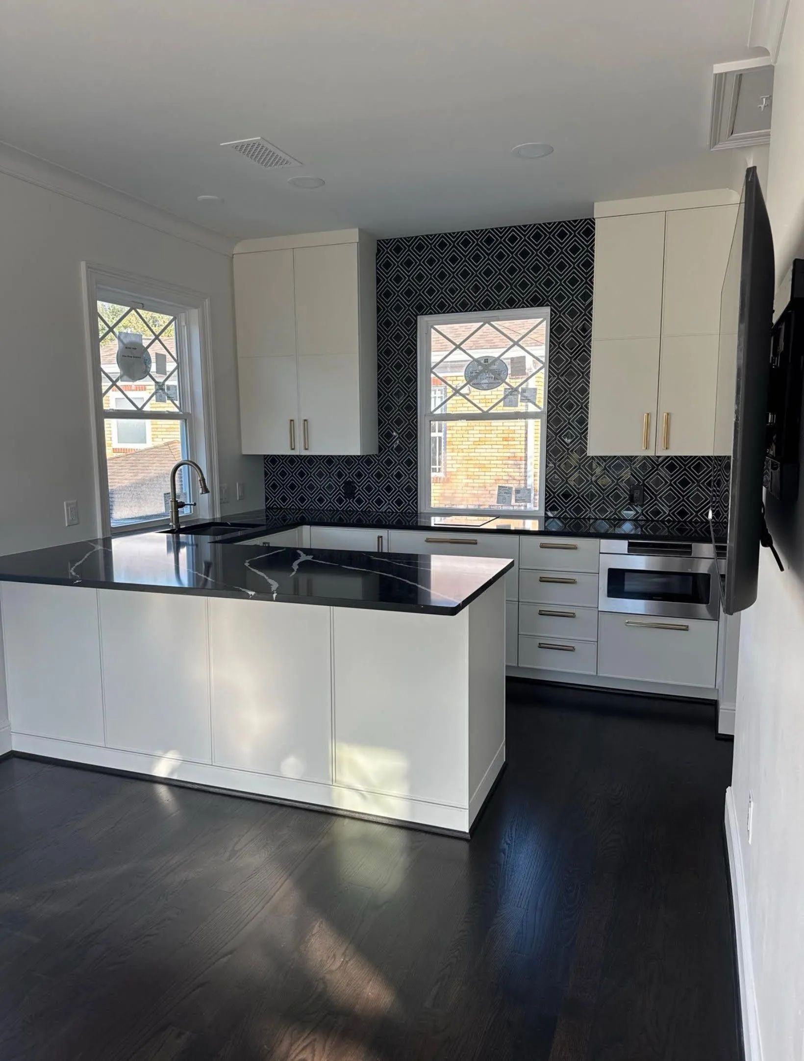 Modern white kitchen with black countertops, dark backsplash, and two windows letting in daylight