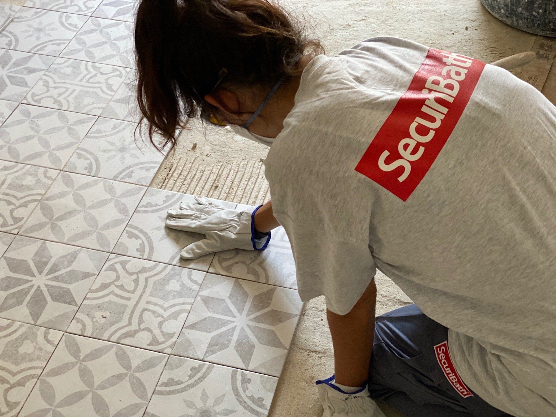 Persona con mascarilla y guantes, colocando baldosas estampadas en el suelo.