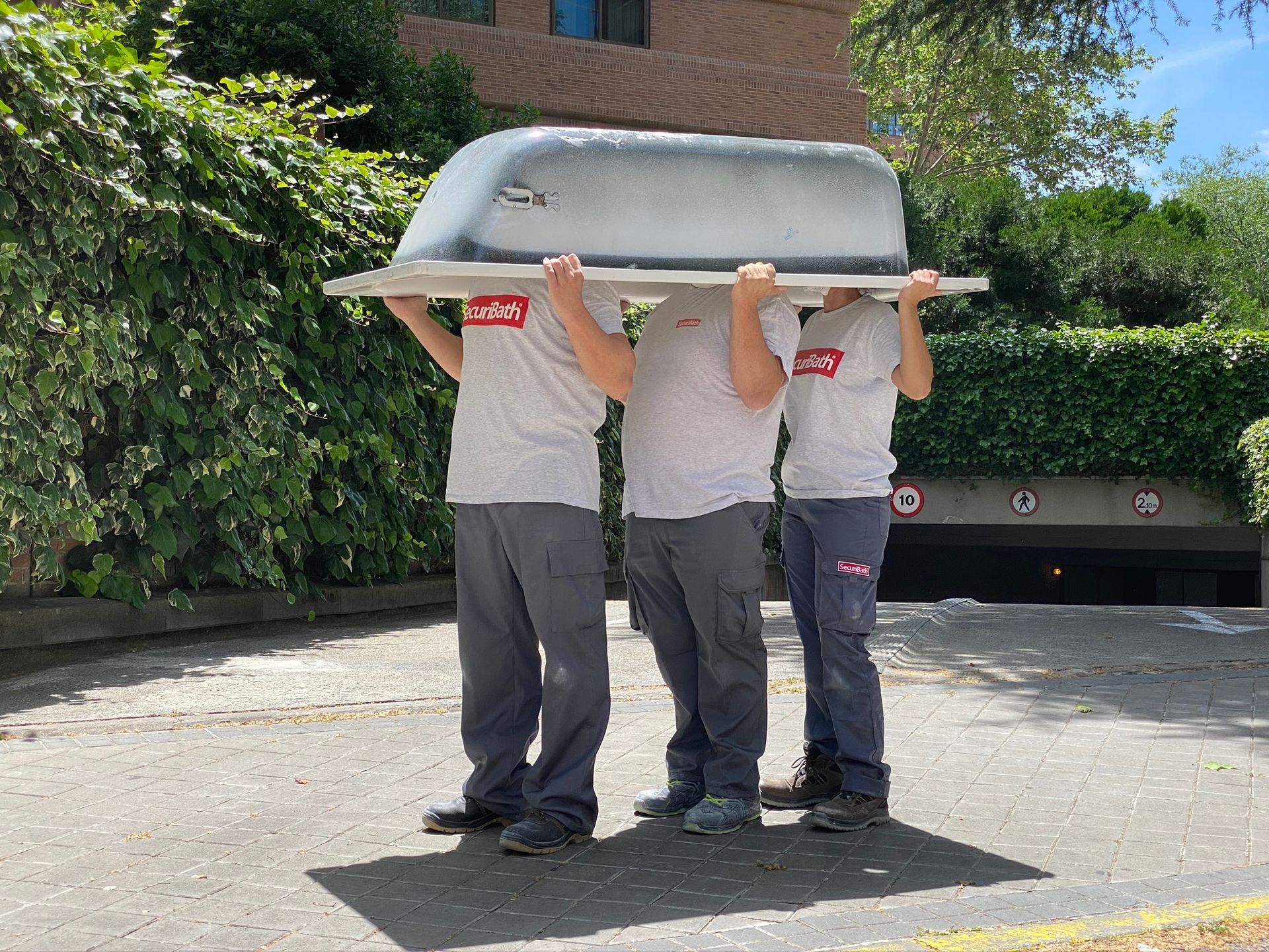 Tres personas vestidas con camisetas grises sacan una bañera grande al exterior.