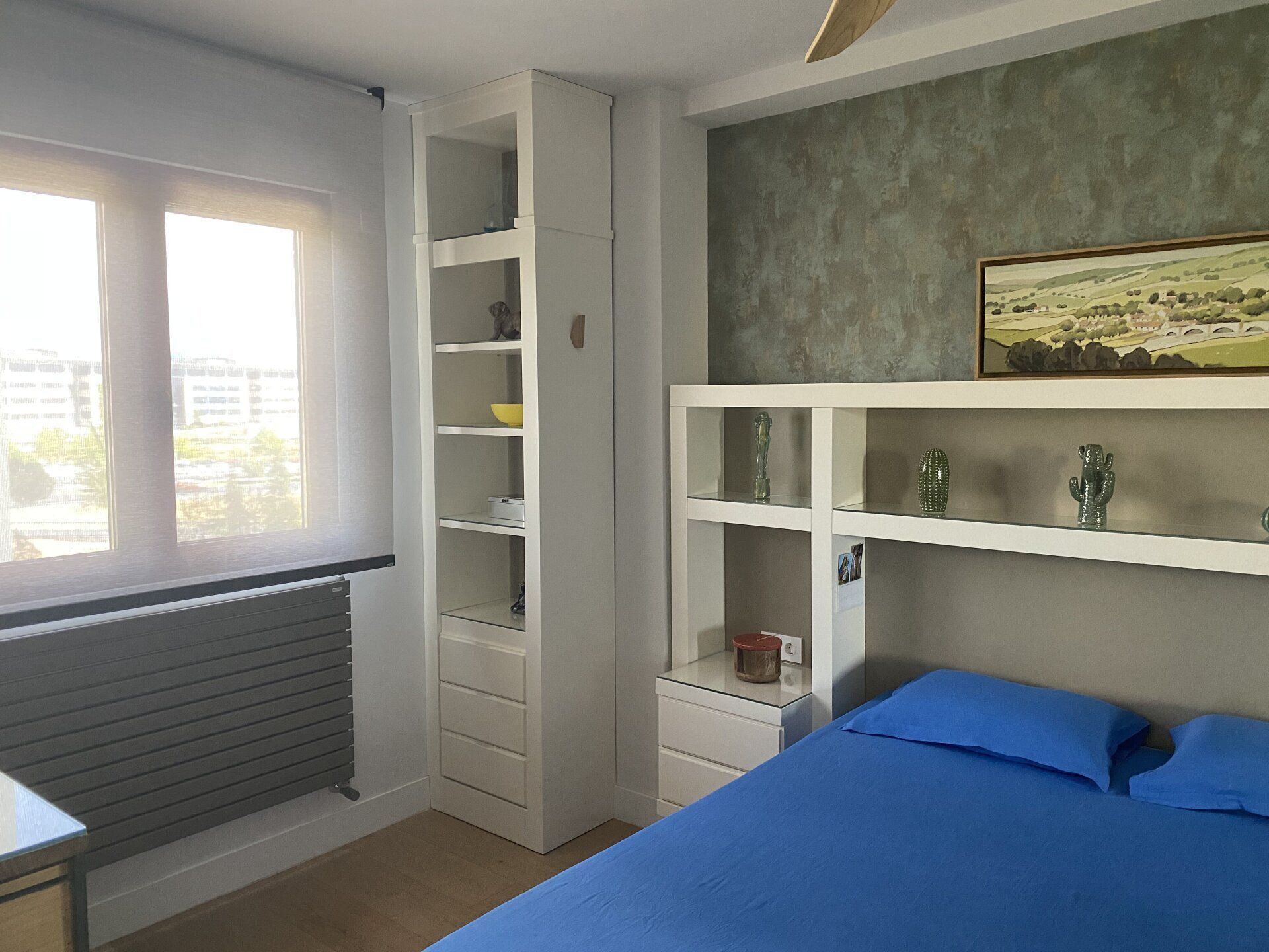 Un dormitorio con cama, mesita de noche, estanterías y ventana.