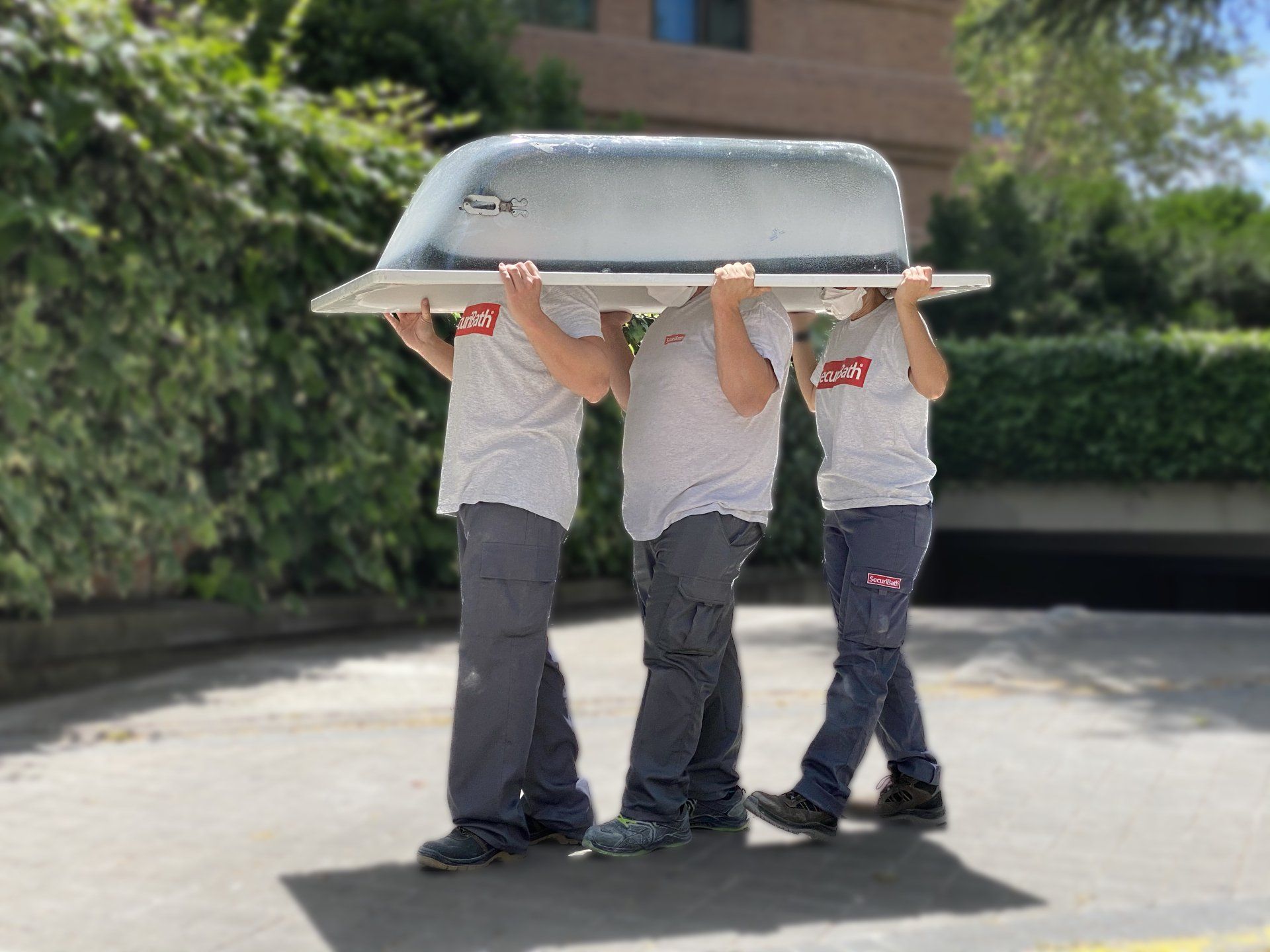 Tres hombres llevan una bañera sobre sus cabezas.