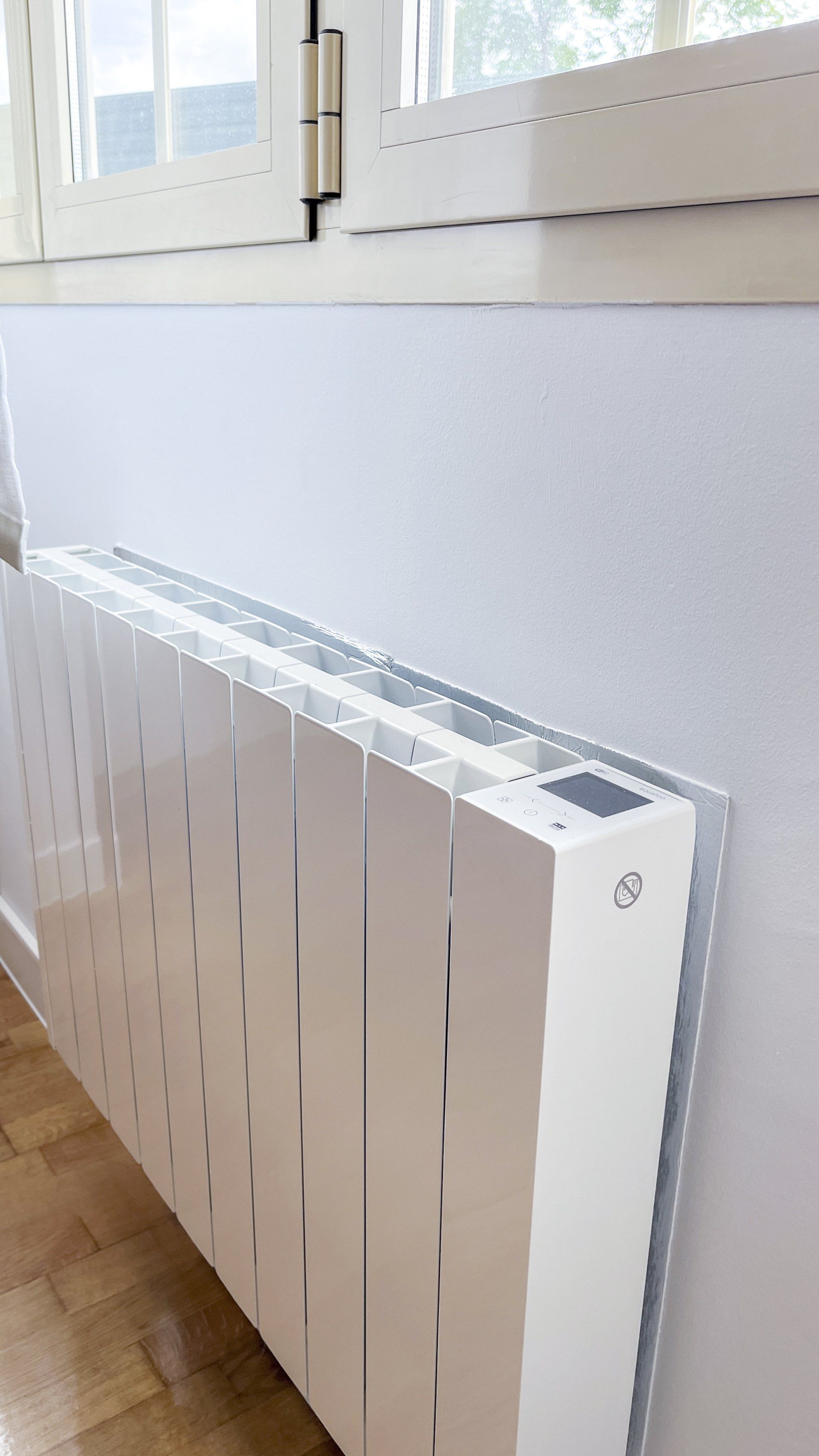 Un radiador blanco está colocado en una pared blanca junto a una ventana.