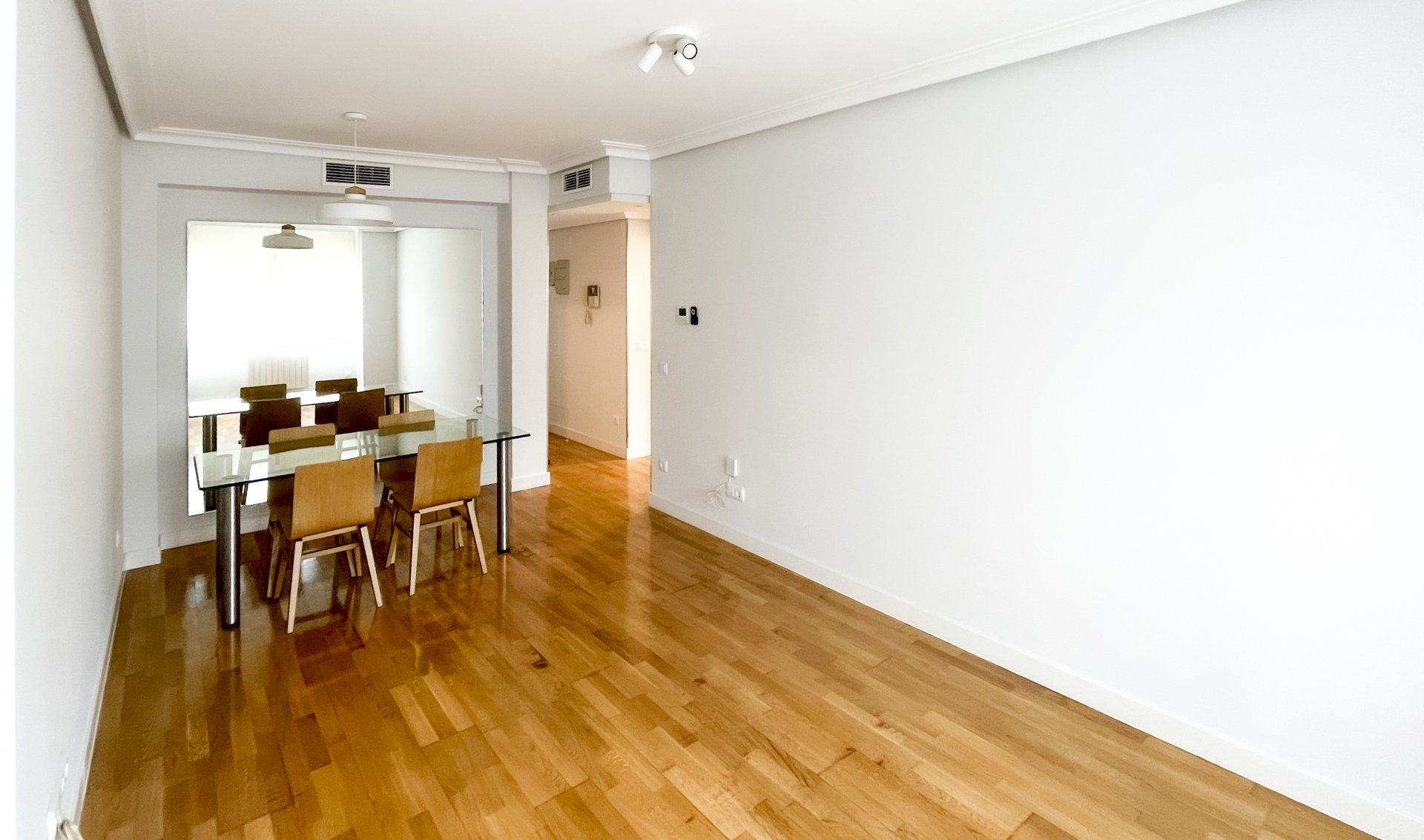 Una habitación vacía con suelo de madera, mesa y sillas.