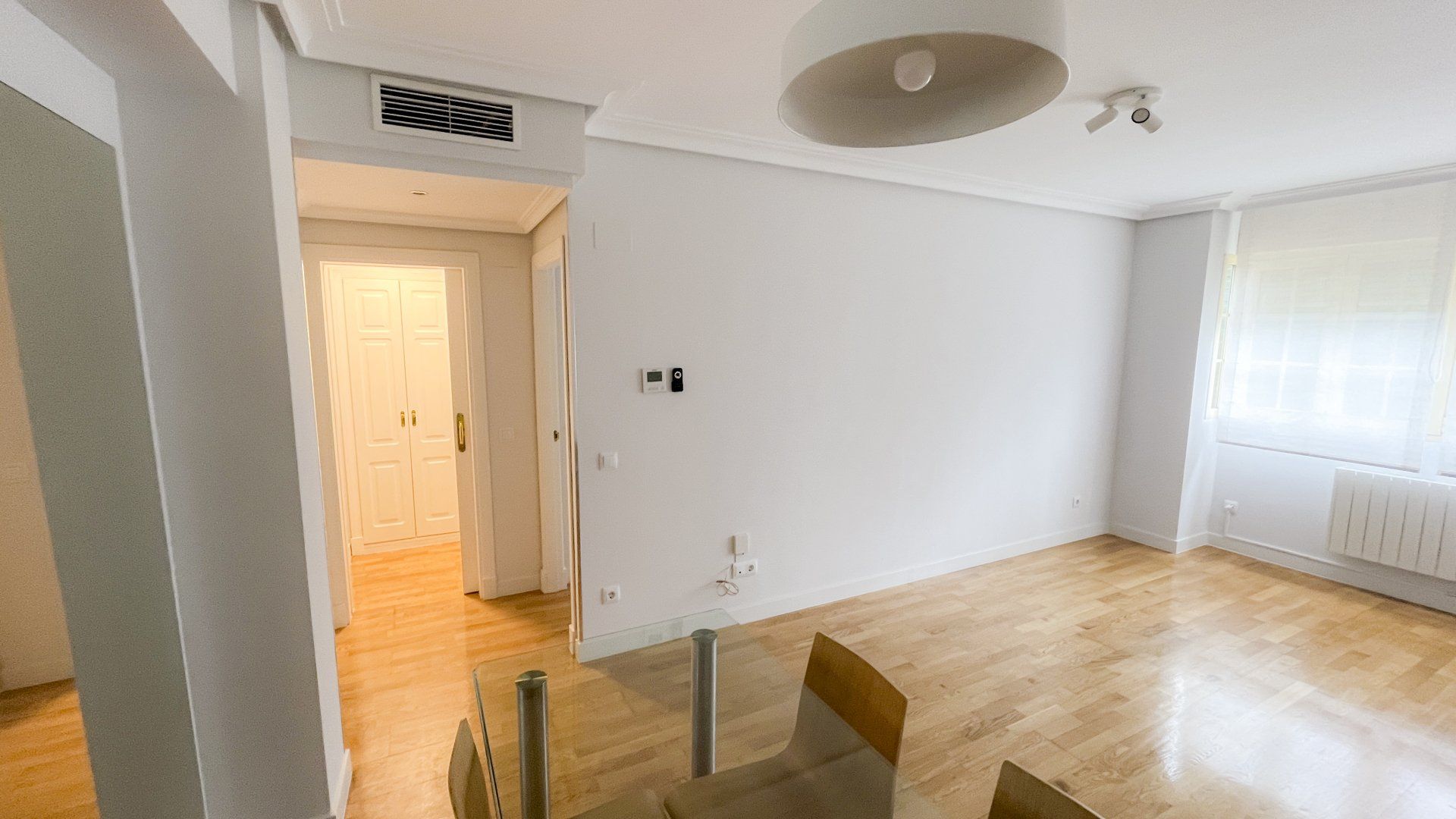 Un salón vacío con una mesa de cristal y sillas.