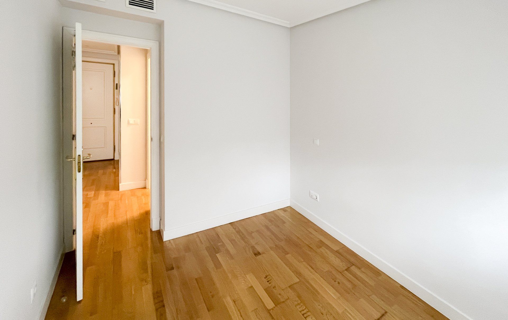Una habitación vacía con suelos de madera y paredes blancas.
