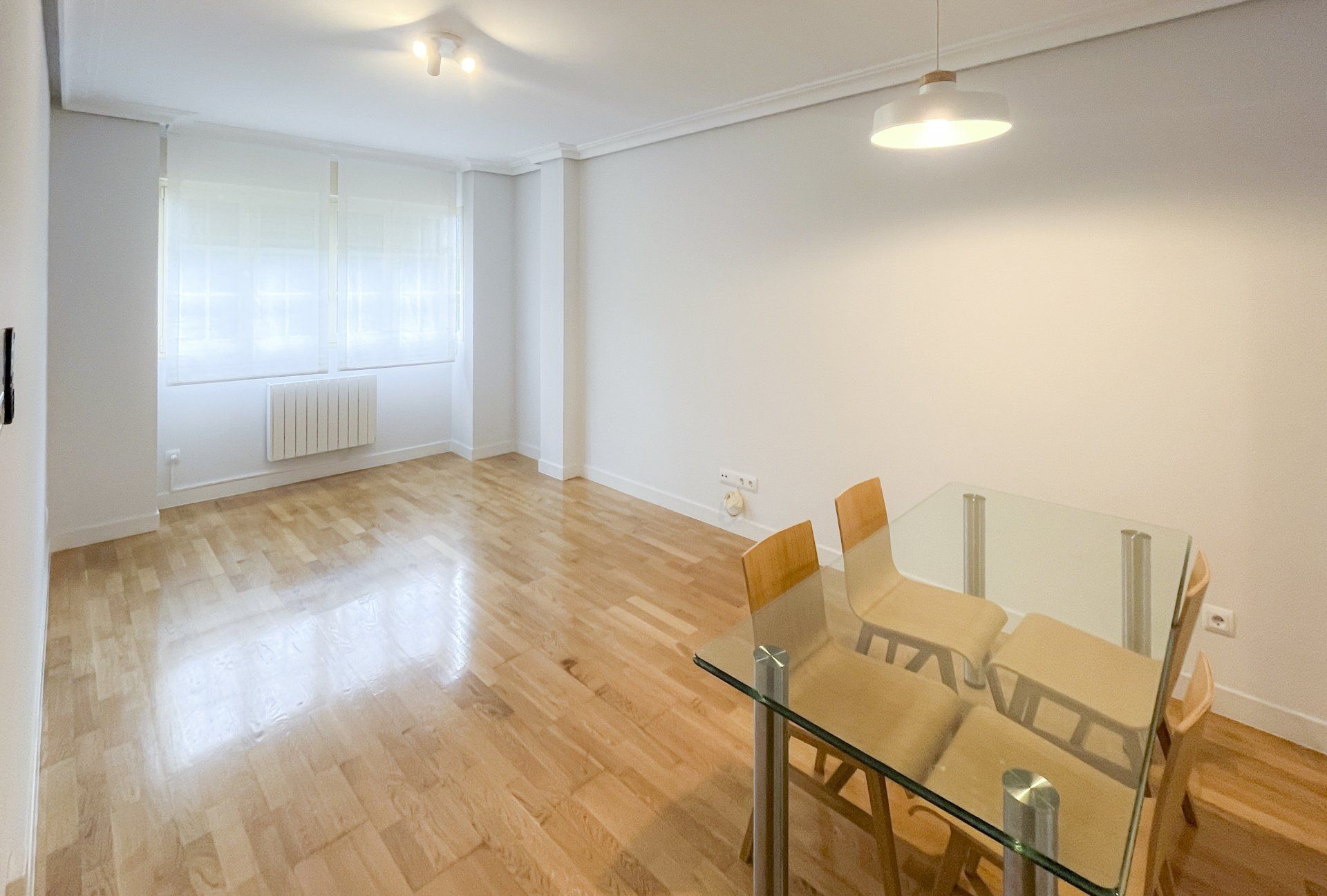 Un salón vacío con una mesa de comedor de cristal y sillas.
