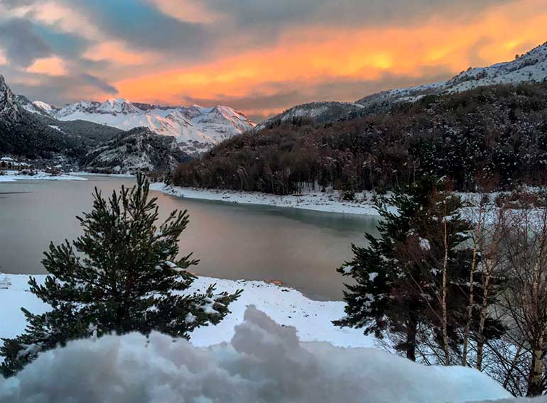 Un lago rodeado de árboles y montañas cubiertos de nieve al atardecer.