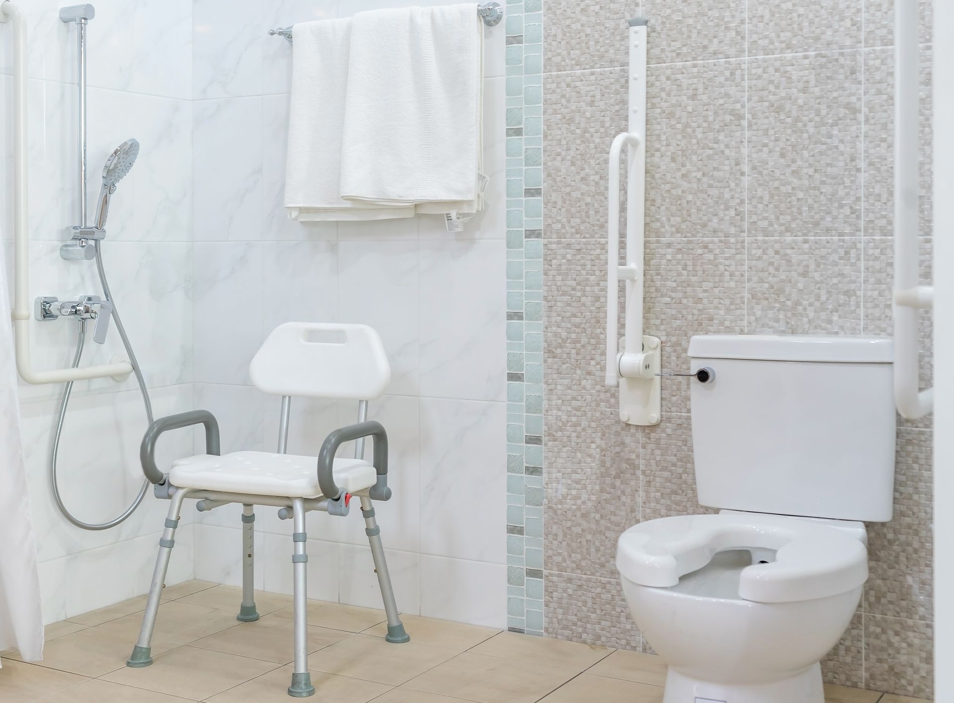 Baño accesible con ducha, barras de apoyo, silla de ducha e inodoro elevado.
