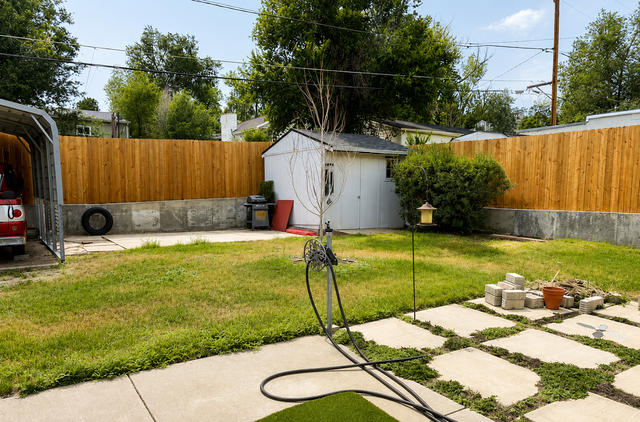 Backyard with grass, stone patio, white shed, and wooden fence on a sunny day