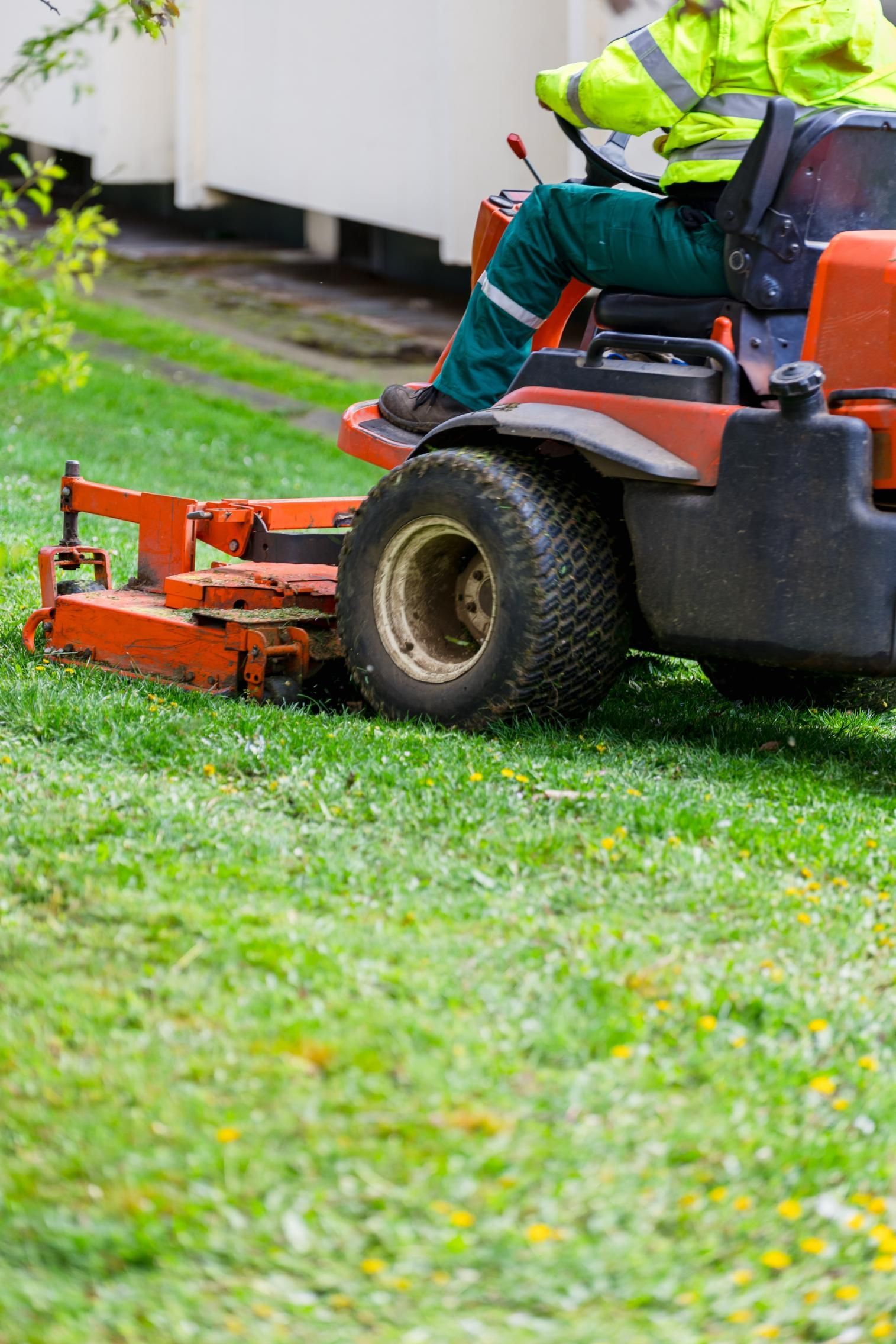 Person operating a red riding lawn mower on a green grassy lawn.