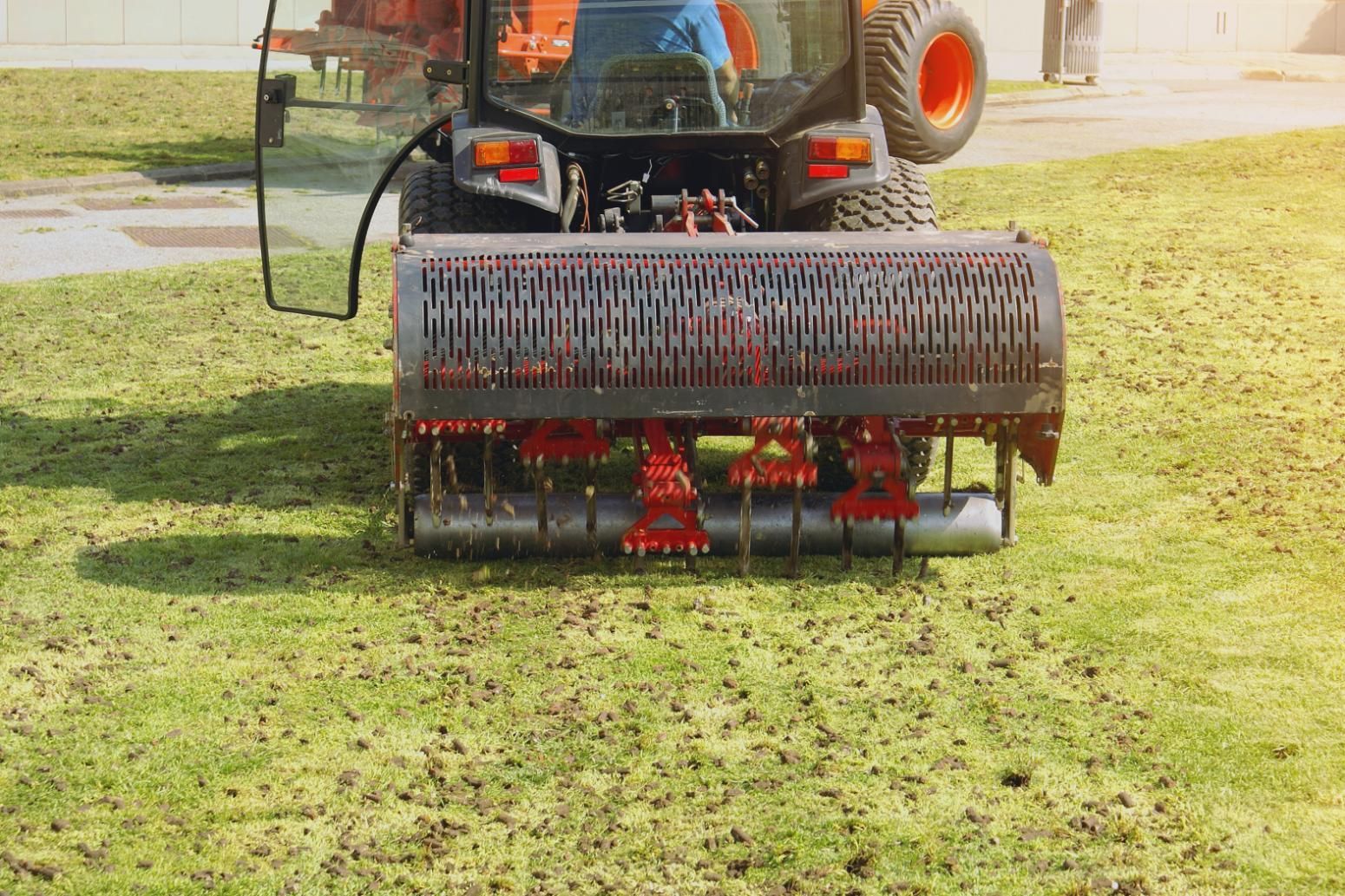 A tractor aerating a grassy field with a large cylindrical implement.