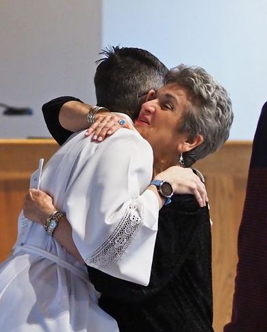 A woman is hugging a pastor in a white alb