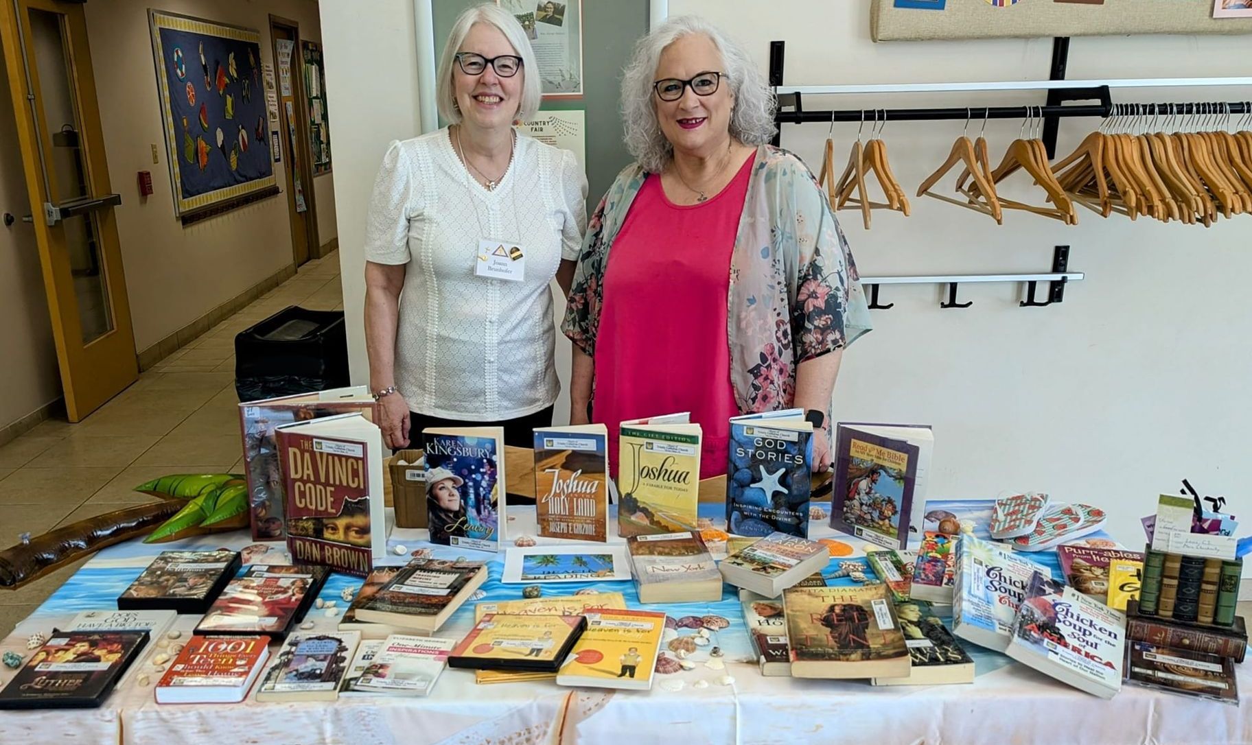 Two women are standing next to a table filled with books.