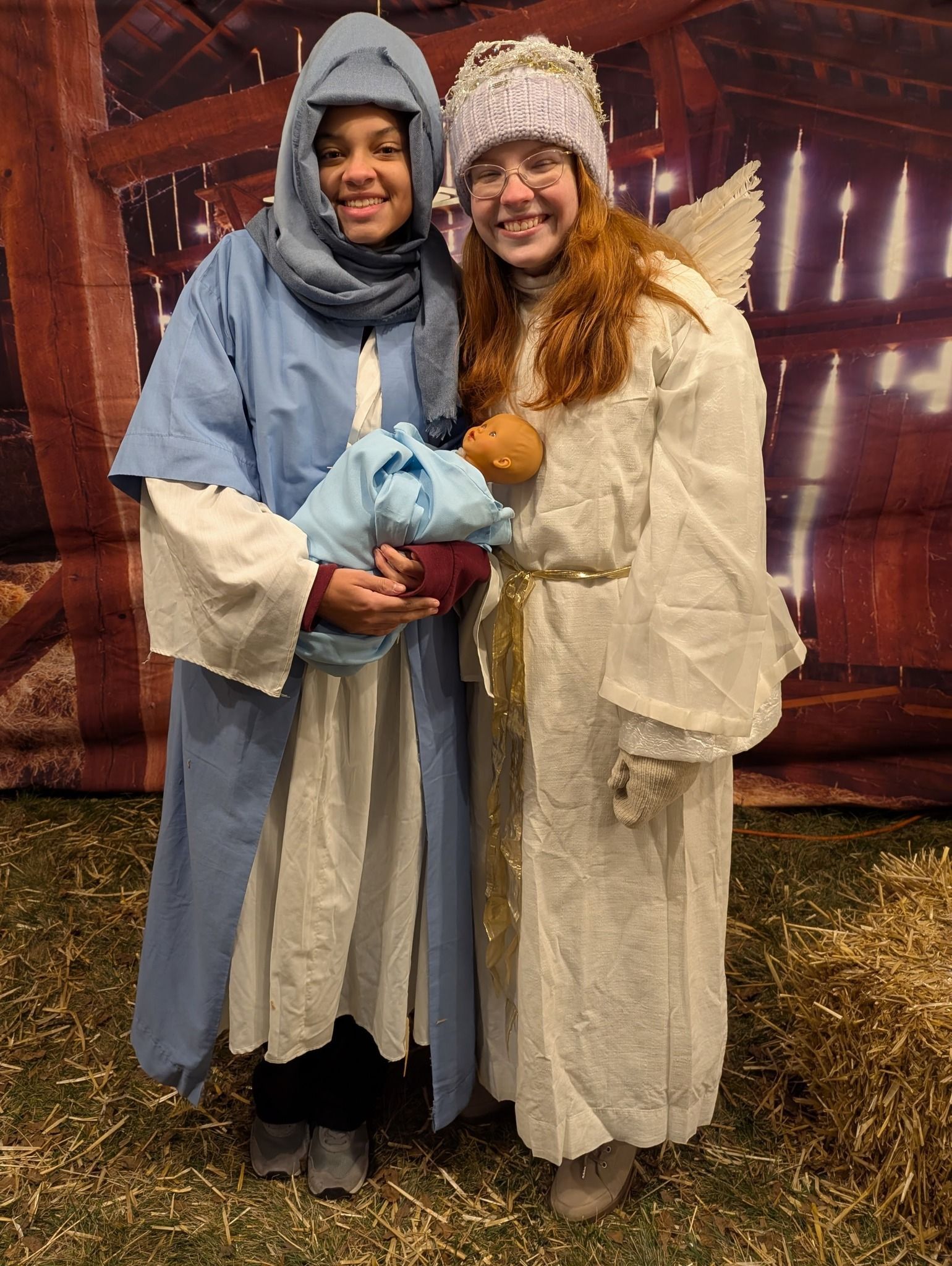 Two teenager dressed in nativity costumes are holding a baby.