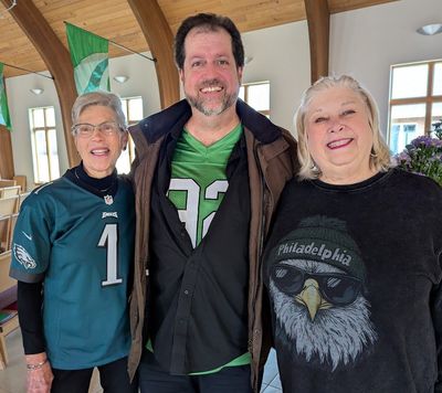 A man and two women wearing Philadelphia Eagles jerseys are posing for a picture.
