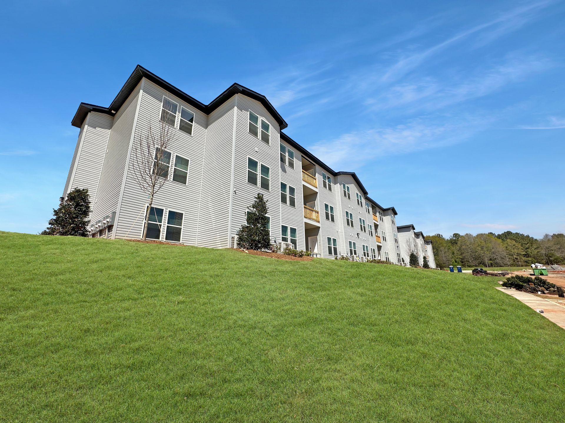 White multi-story apartment building on a grassy hill under a blue sky
