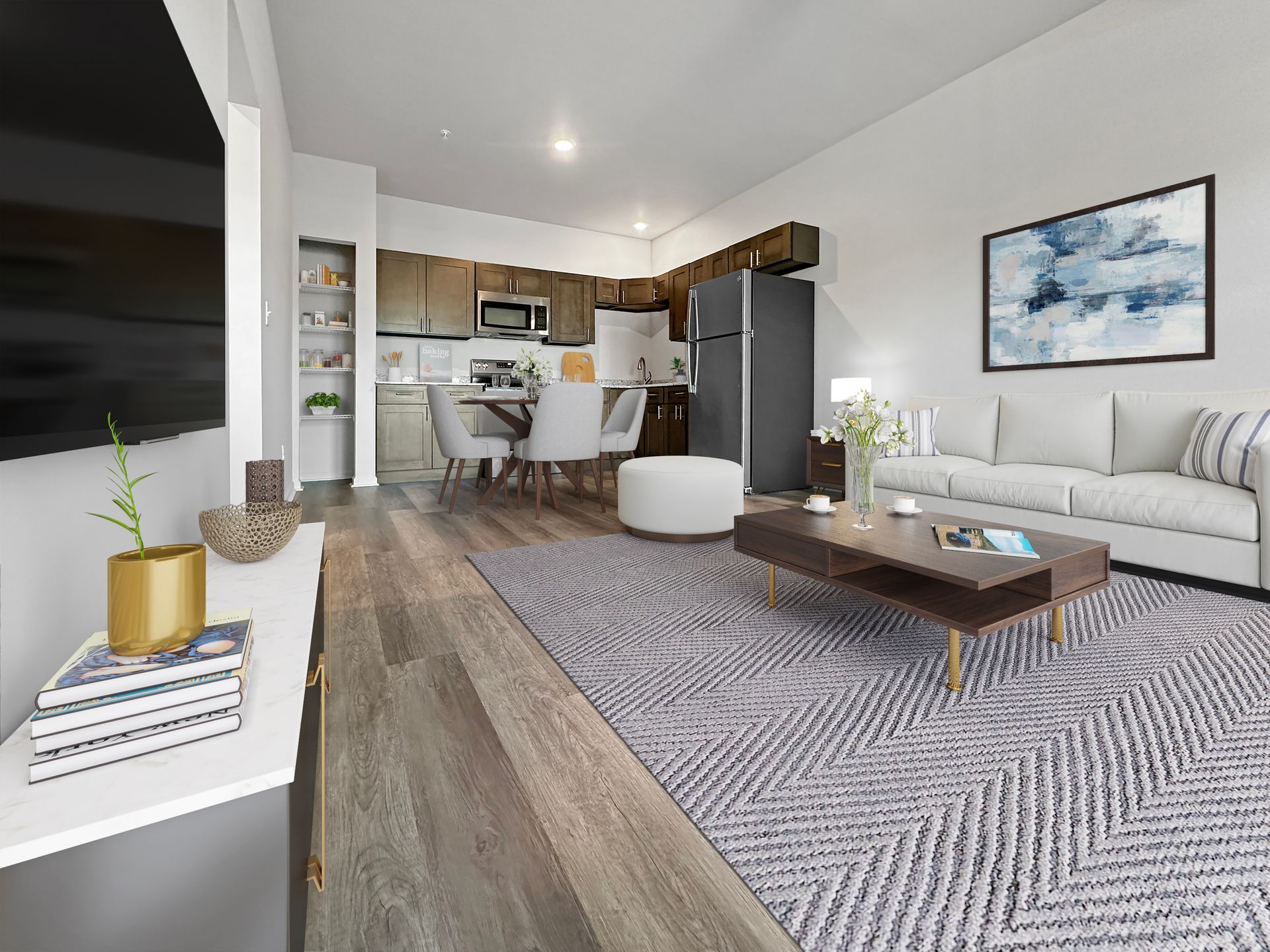 Modern open-plan living room and kitchen with gray sofa, wood floors, patterned rug, and white cabinets