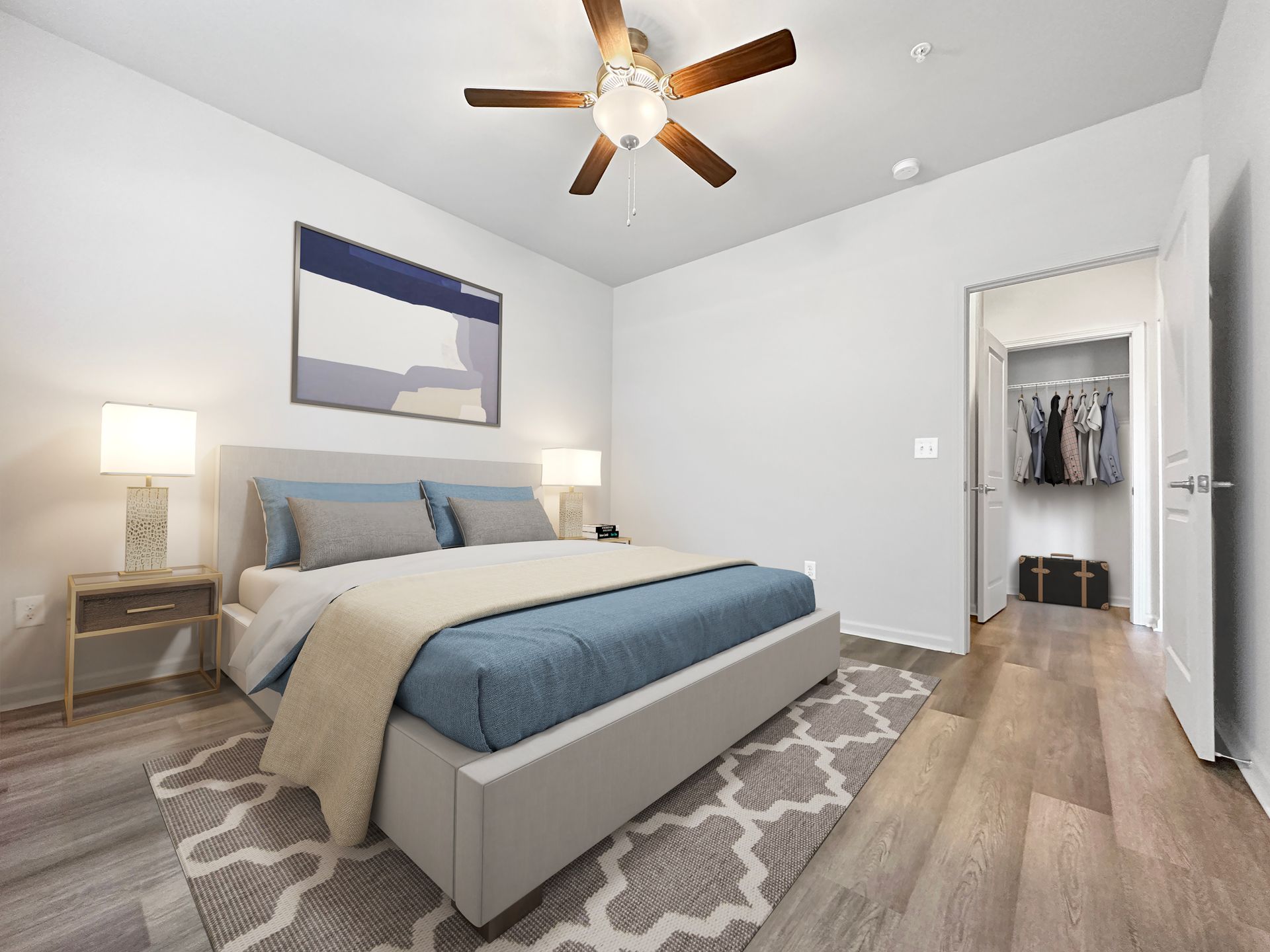 Bright modern bedroom with gray bed, patterned rug, nightstand lamp, ceiling fan, and open closet.