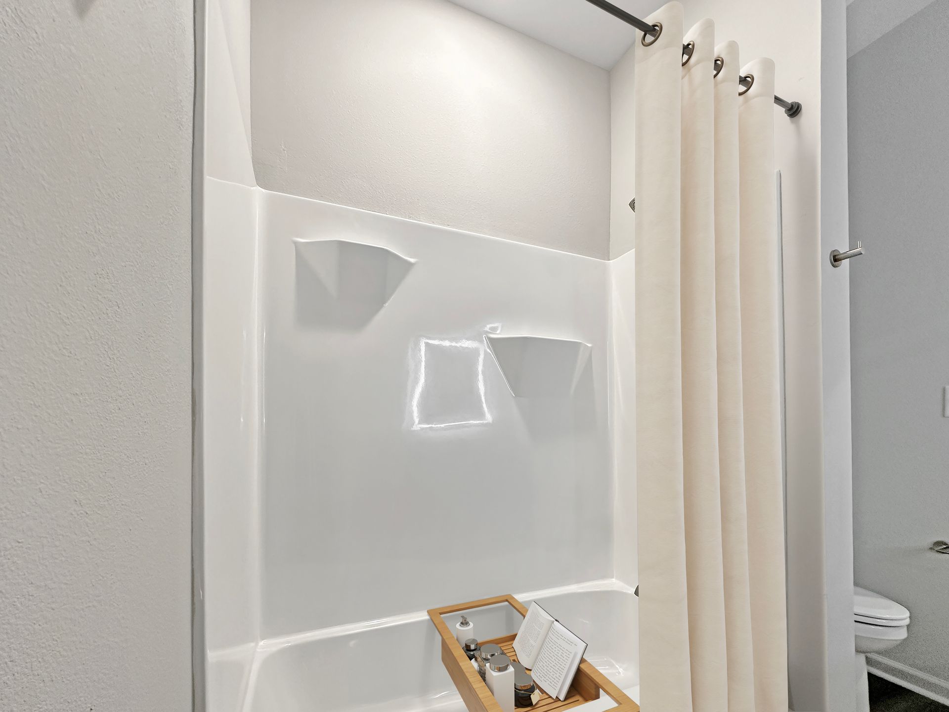 Minimalist bathroom shower with white curtain, glossy wall tiles, and a wooden caddy on the floor