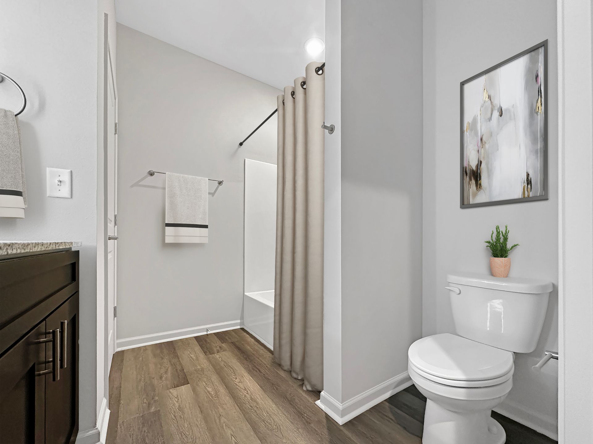 Bright bathroom with shower curtain, wood floor, vanity, and a toilet under framed wall art.