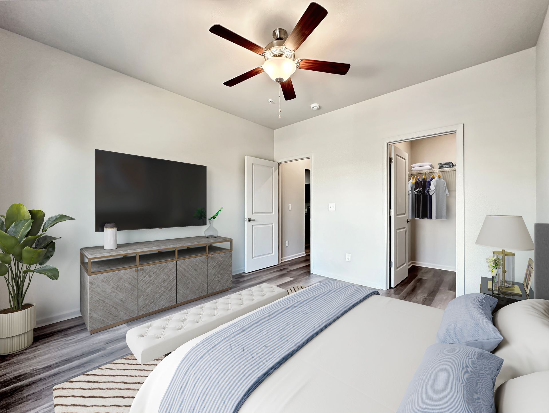 Bright bedroom with a gray bed, TV on a dresser, ceiling fan, and open closet doors