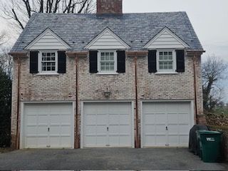 A Large Brick House With Three Garage Doors And Black Shutters — Lititz, PA — Trailside Spouting, LLC