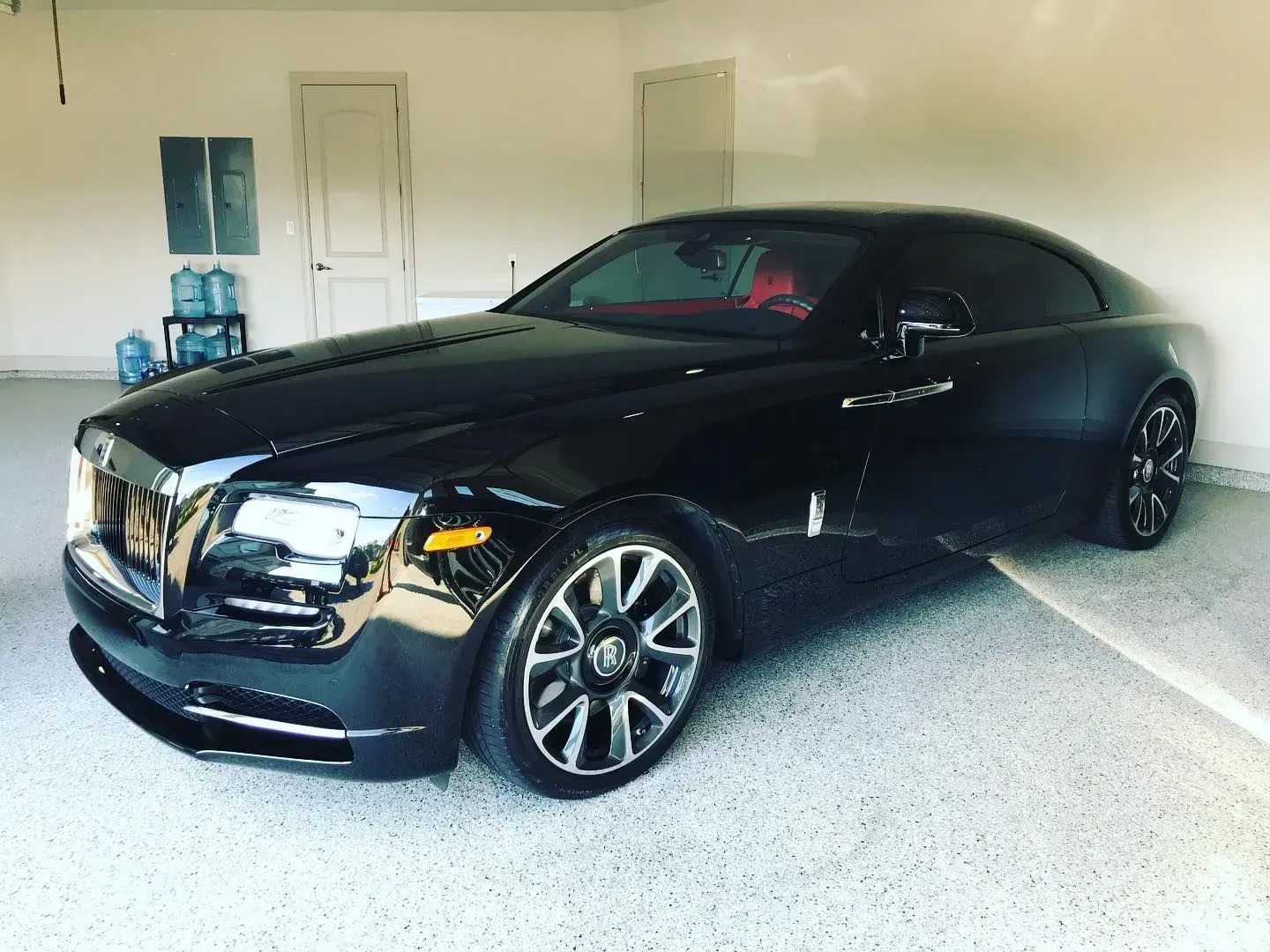 Black luxury sedan parked in a garage, angled front-left view, with polished chrome wheels.