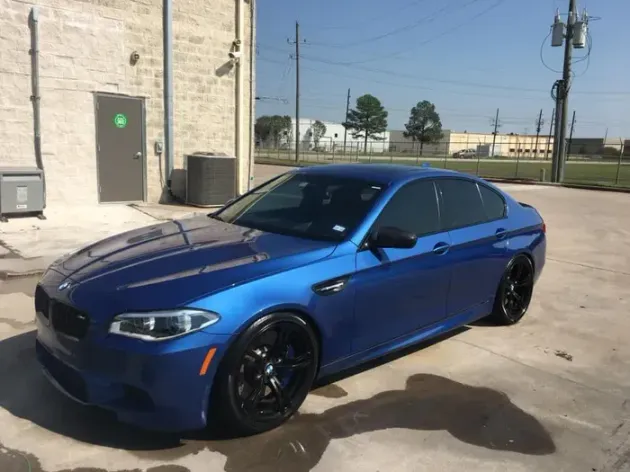 Blue sedan parked beside a beige building in an industrial lot.
