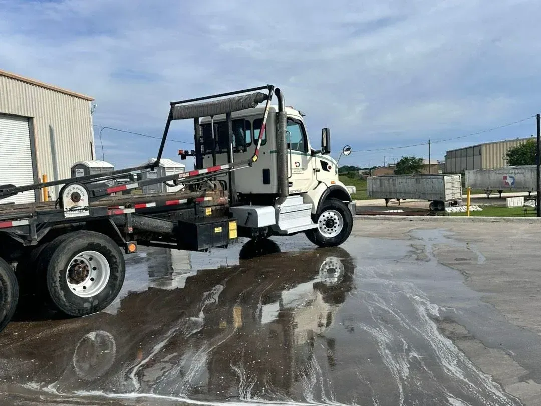 Tow truck hauling a white utility vehicle across a wet lot with reflections