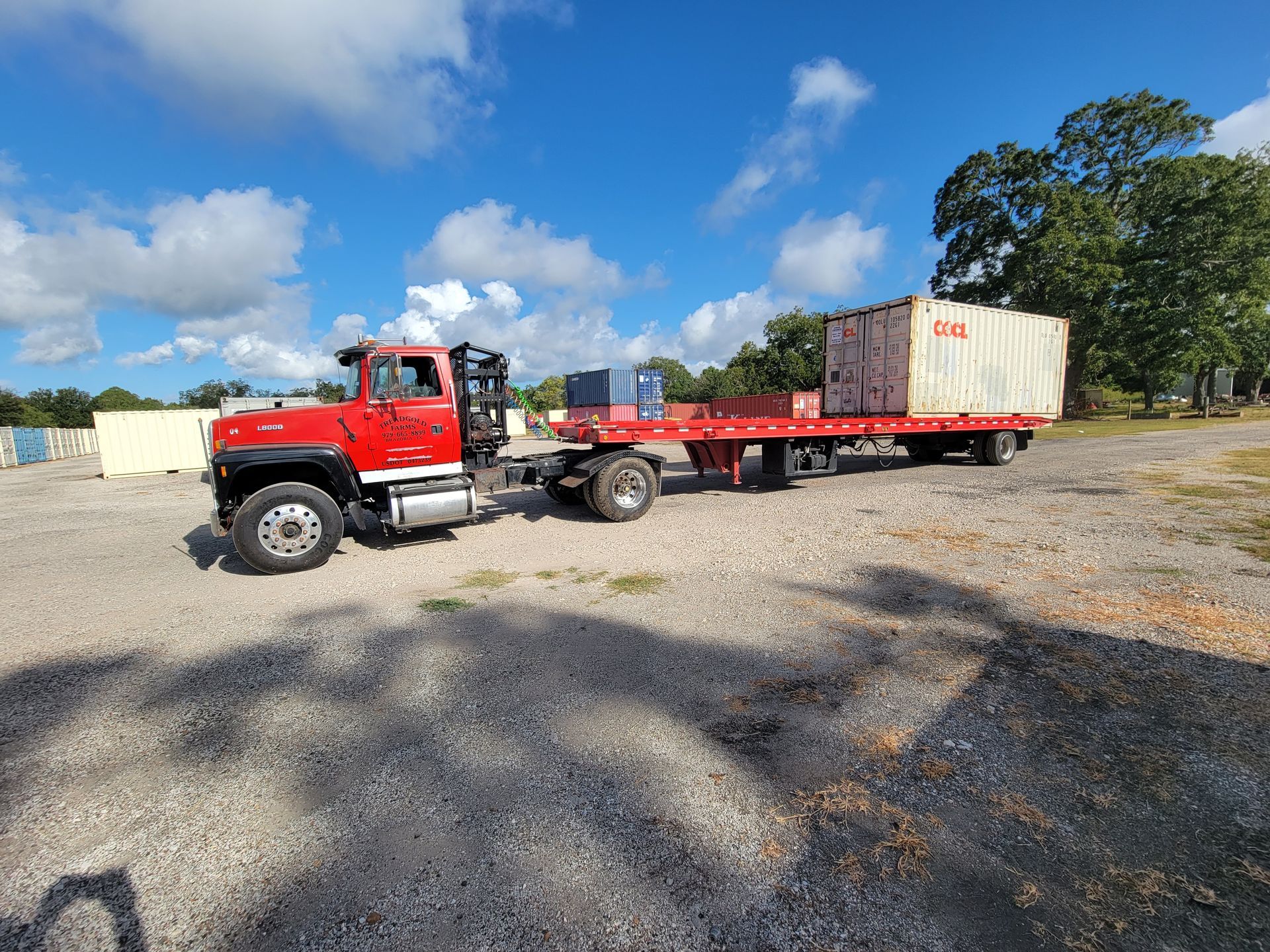 Red flatbed truck carrying pallets on a gravel lot under a blue sky