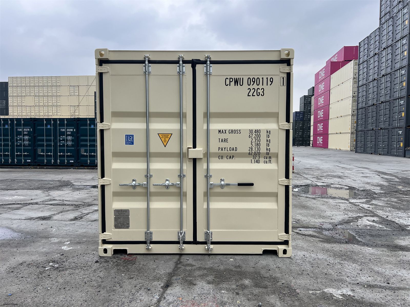 Beige shipping container centered in an industrial yard, with stacked containers in the background.