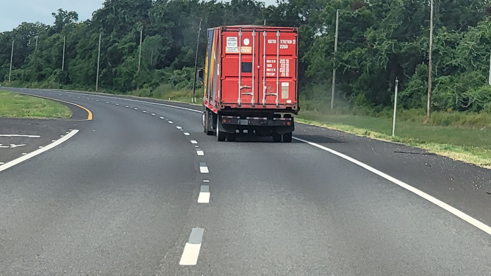 Red shipping truck driving on a curving highway bordered by trees.