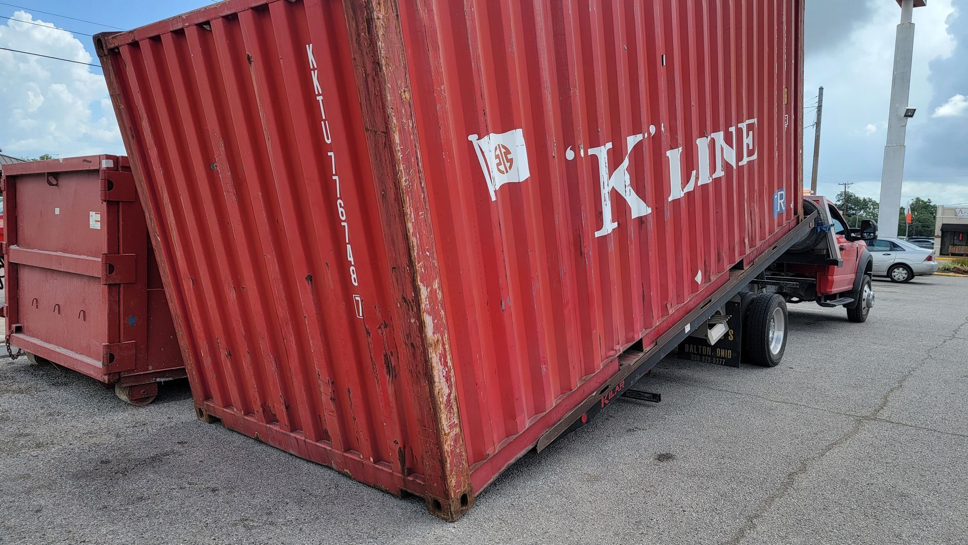 Overturned red K Line shipping container blocking a roadway near a forklift