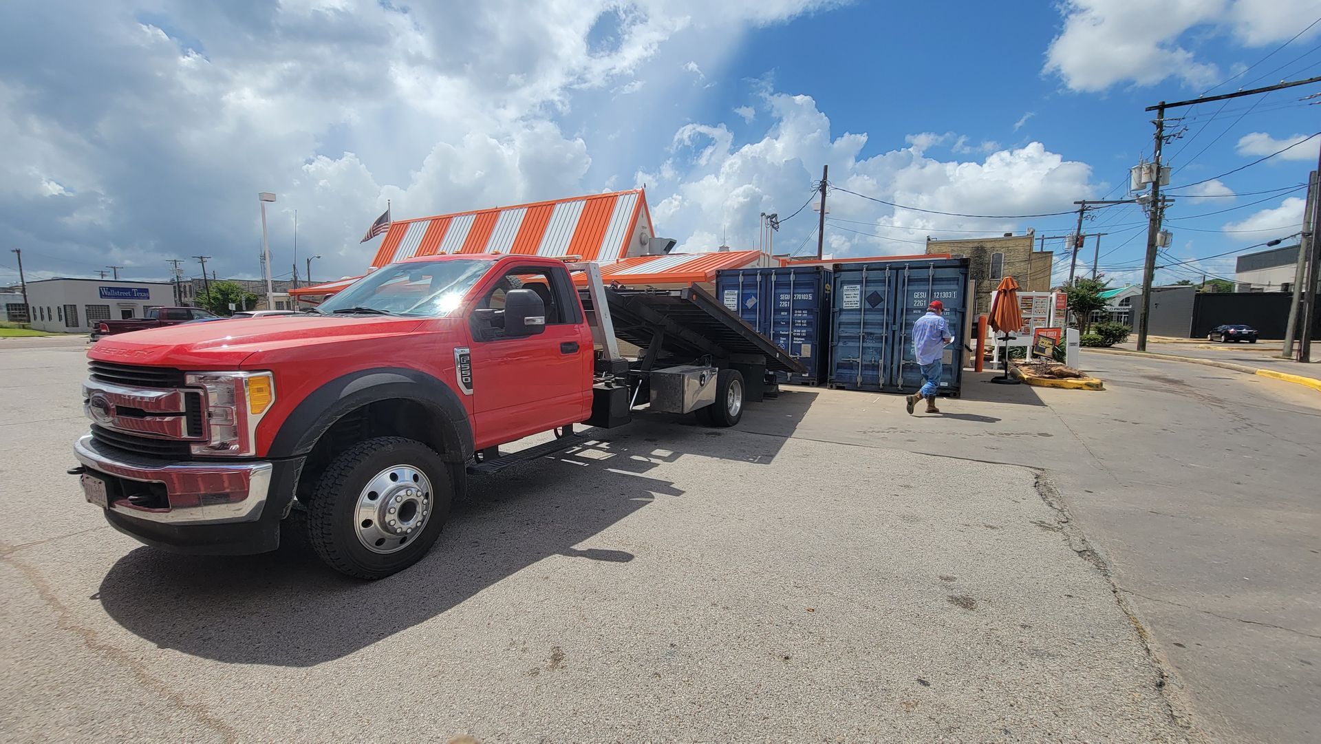 Red tow truck beside a striped canopy at a roadside lot, with a person standing nearby.