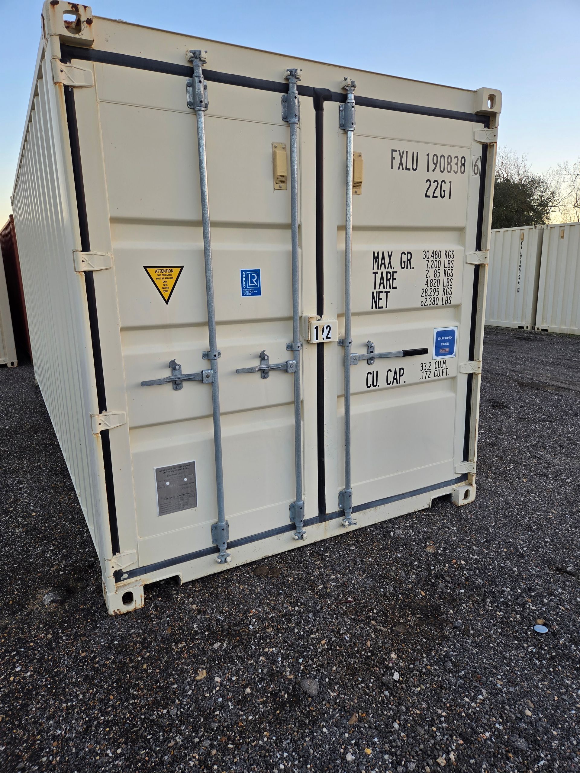 White shipping container with warning labels, sitting on gravel outdoors.