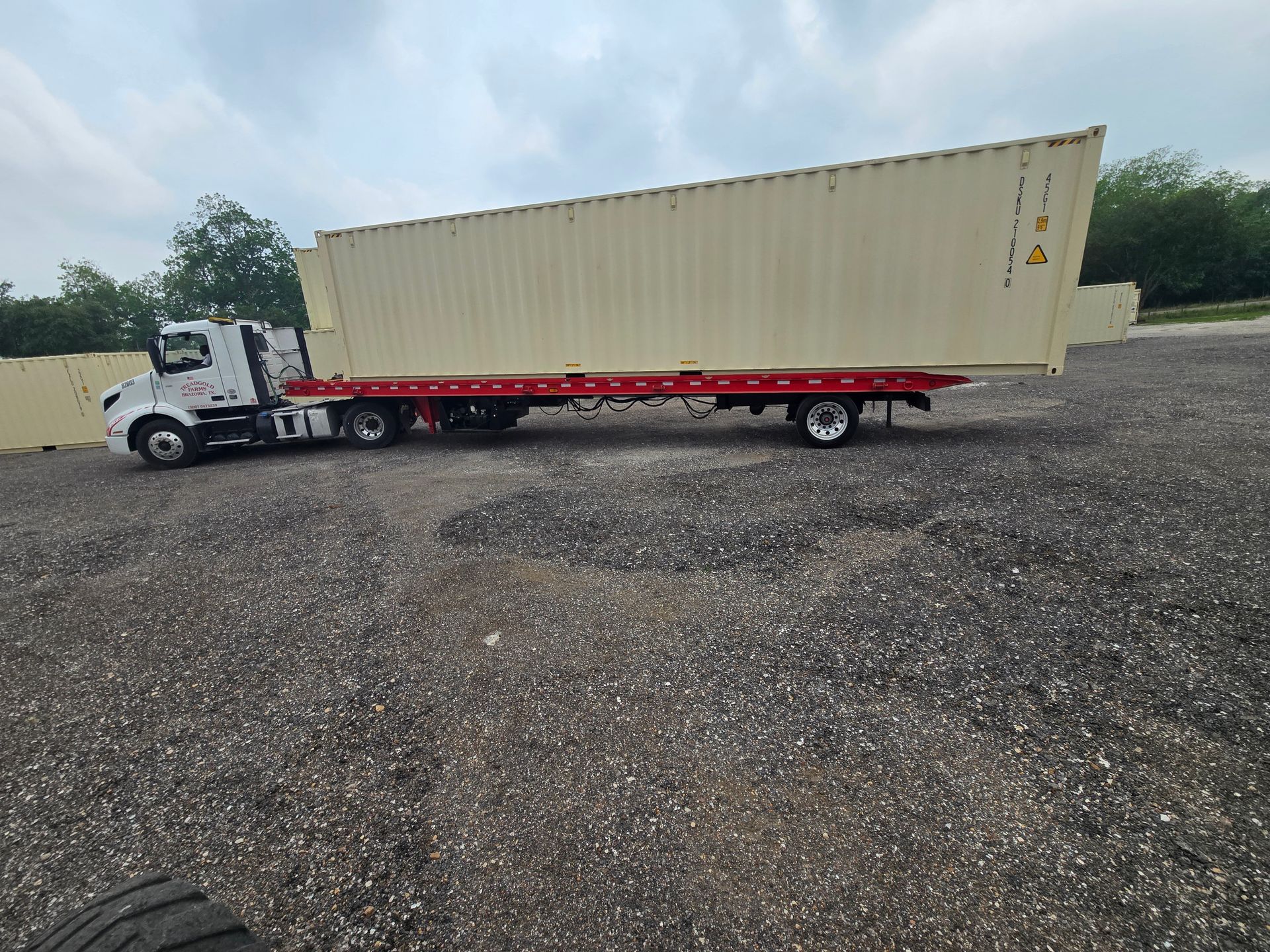 White semi-truck with beige trailer parked on gravel lot under cloudy sky