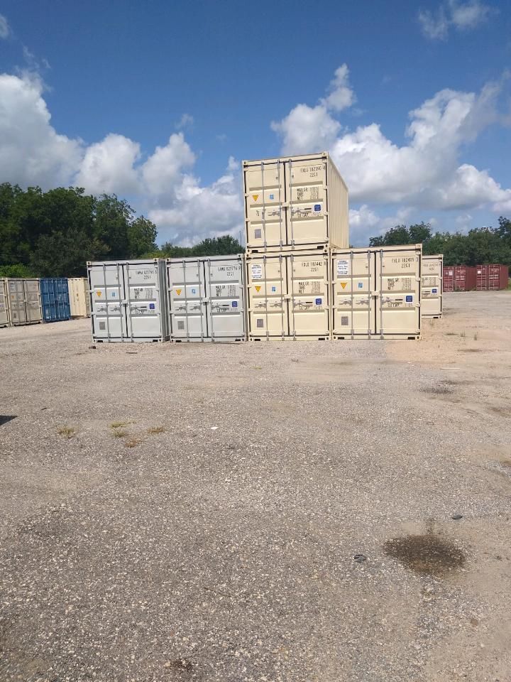 Stacked shipping containers in a gravel lot under a partly cloudy sky.