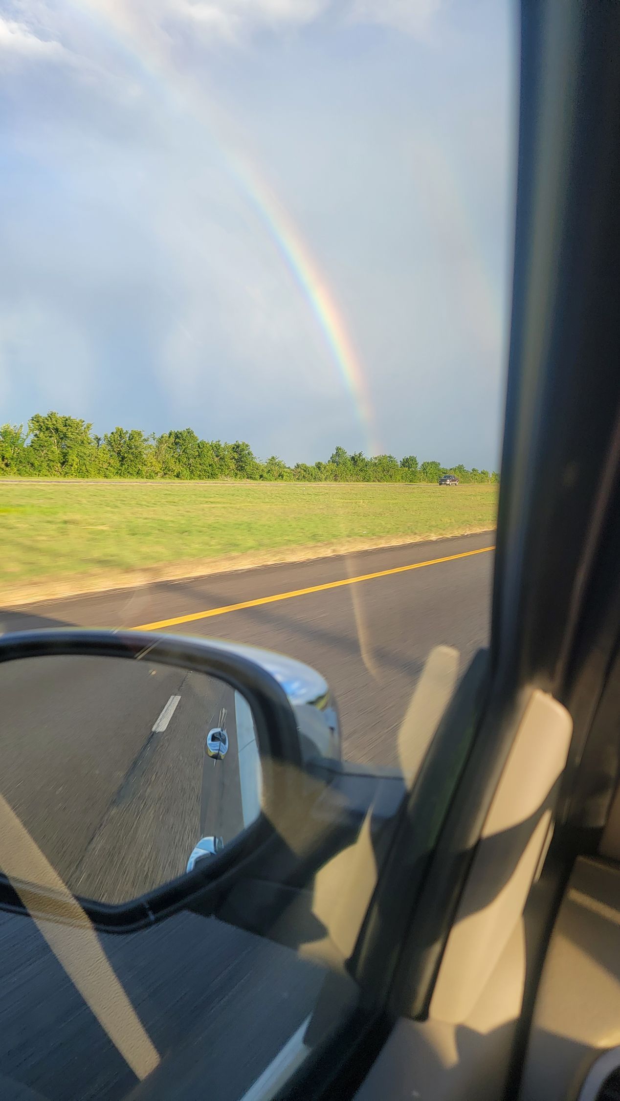 Rainbow over a rural highway seen from a car window with side mirror in view
