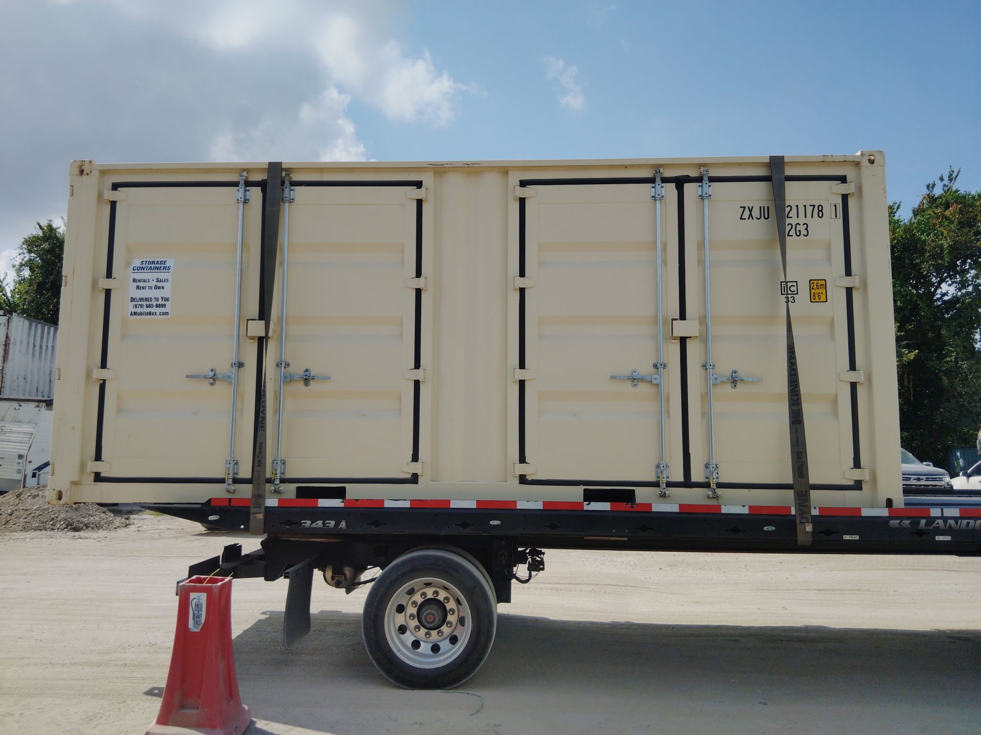 Red shipping container on gravel lot with two people nearby and a beige container in the background