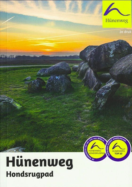 Omslag van een reisgids met de titel "Hünenweg" (Hondenweg) met stenen op een grasveld bij zonsondergang.