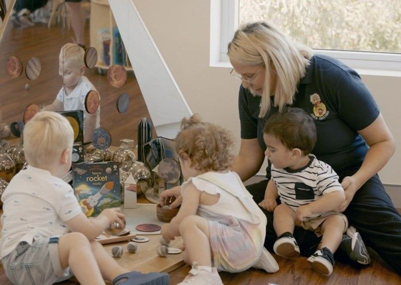 A Woman Is Sitting on The Floor Playing with Three Children — Shell Heights, NSW — Junior Einsteins A woman is sitting on the floor playing with three children.
