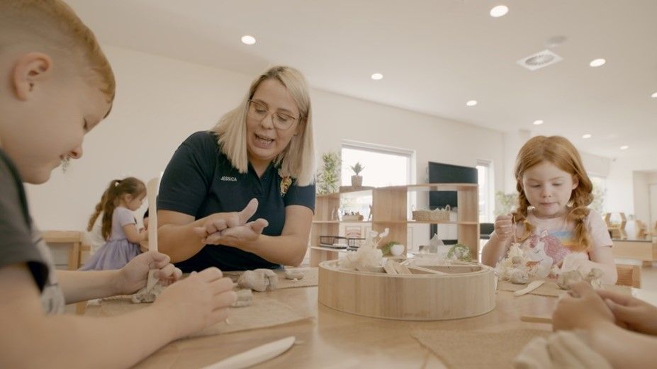 A Woman Is Teaching Children how To Make Clay — Shell Heights, NSW — Junior Einsteins A woman is teaching children how to make clay in a classroom.