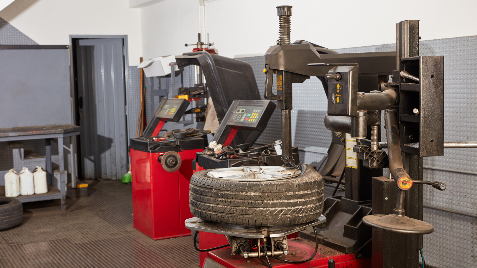 Industrial workshop with red and black tire-changing machines and stacked tires on a tiled floor.