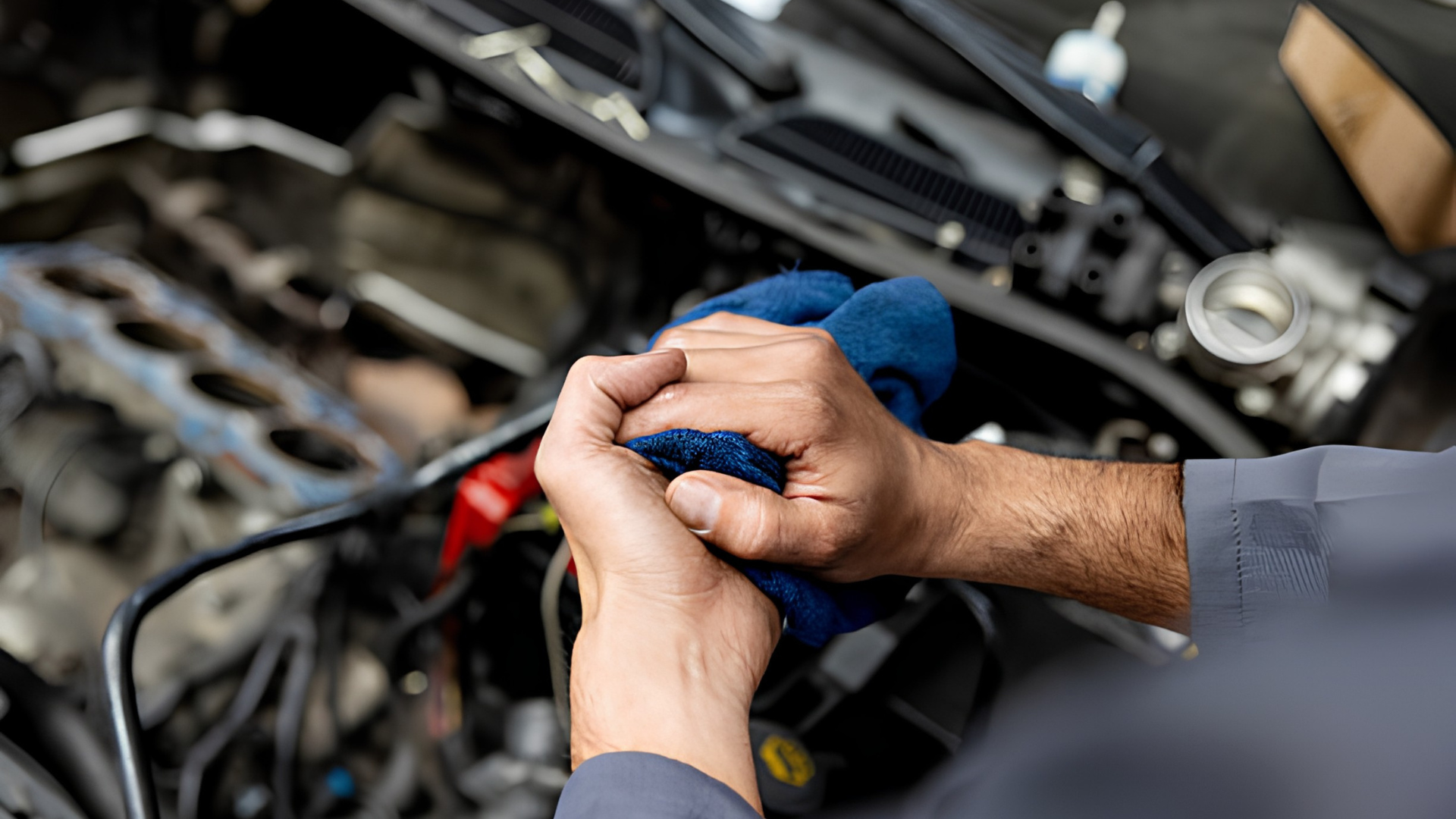 Hands using a blue cloth to work on a car engine in a garage