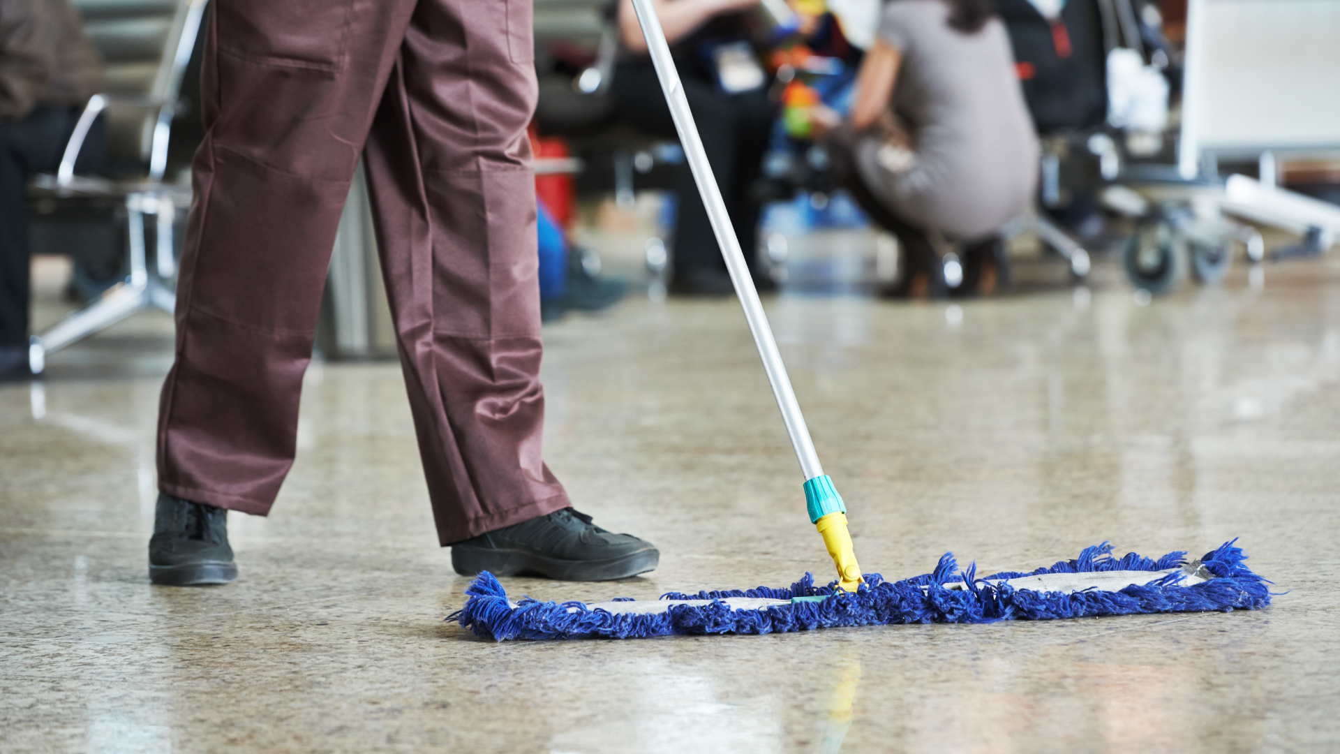 Person mopping a glossy floor with a blue mop in a busy indoor space