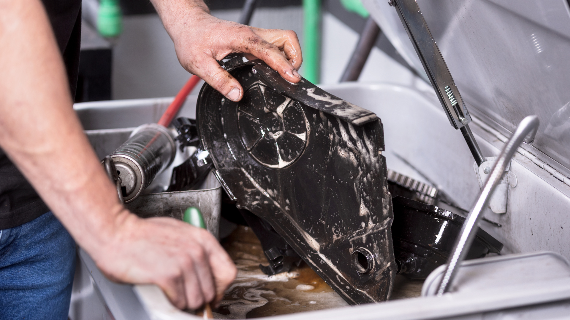 Hands washing a black pan in a kitchen sink with running water.