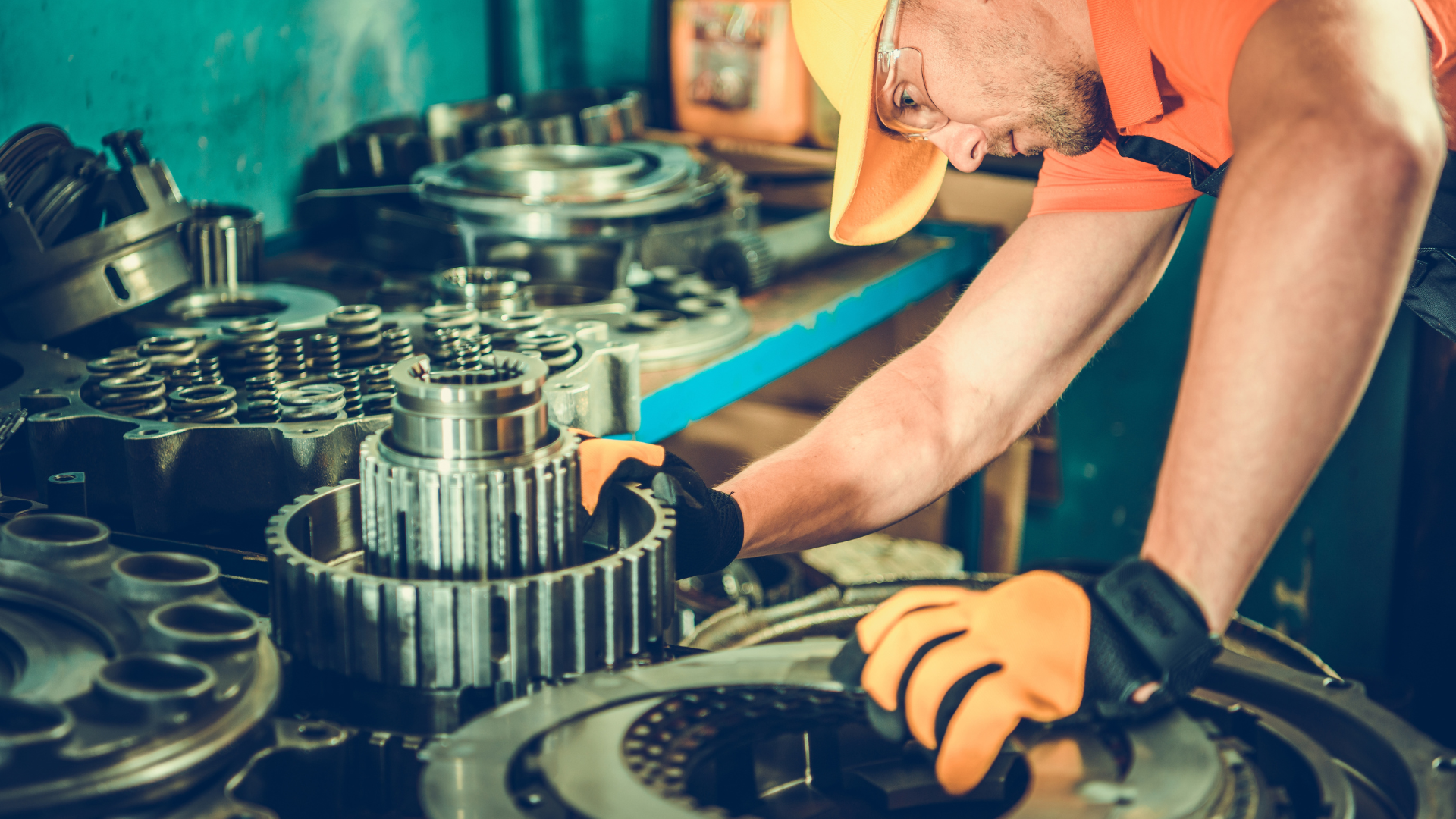 Mechanic in orange shirt working on exposed gears and machinery in a workshop