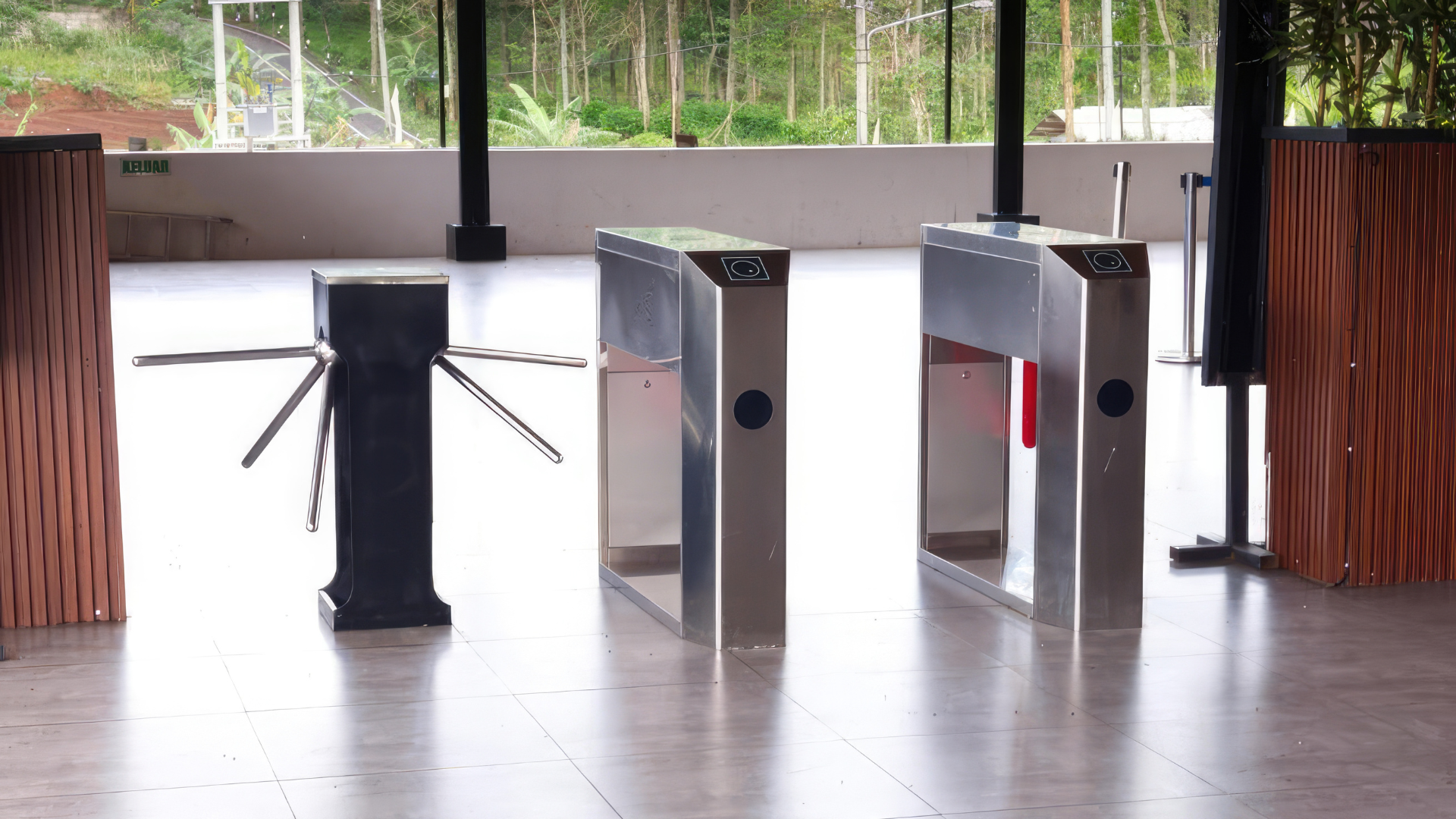 Three stainless-steel turnstiles in a building entrance lobby with glass doors behind them.